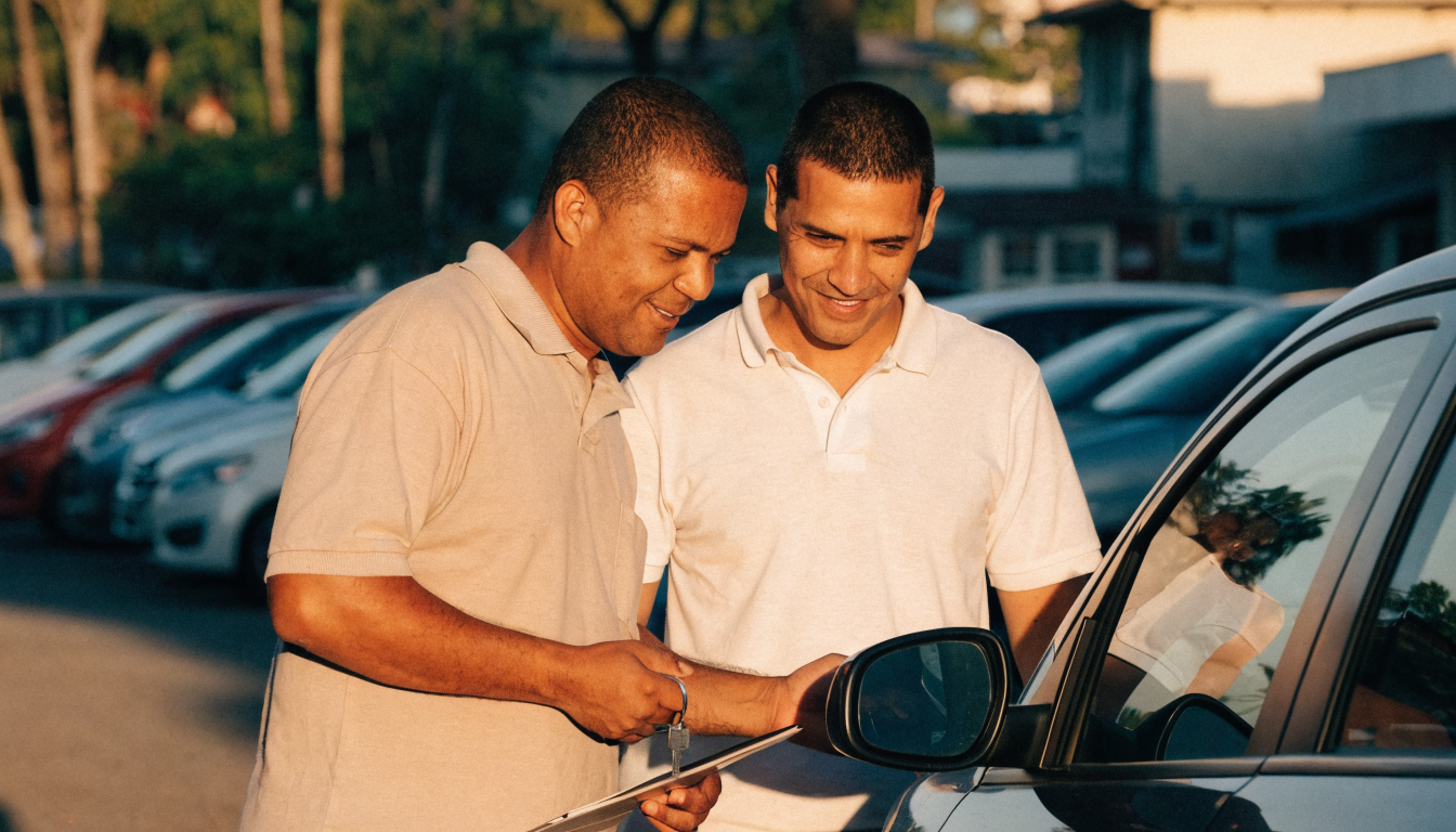 Dois profissionais conversam sorrindo enquanto observam um carro em um pátio de revenda.